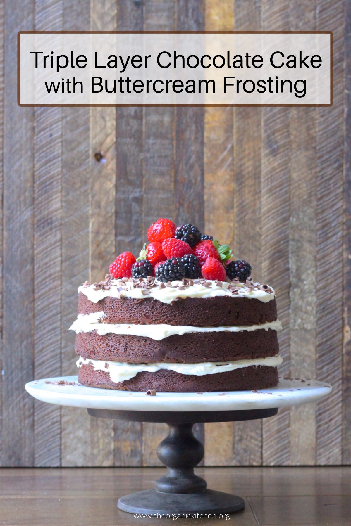 Triple Layer Naked Chocolate Cake with Buttercream Frosting A Triple Layer Naked Chocolate Cake with Buttercream Frosting topped with berries on a cake plate in front of a wooden backdrop