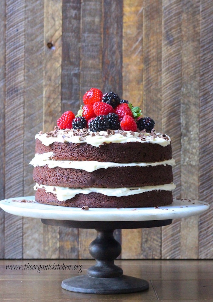 A triple layer Naked Chocolate Cake with Buttercream Frosting topped with colorful berries on cake plate