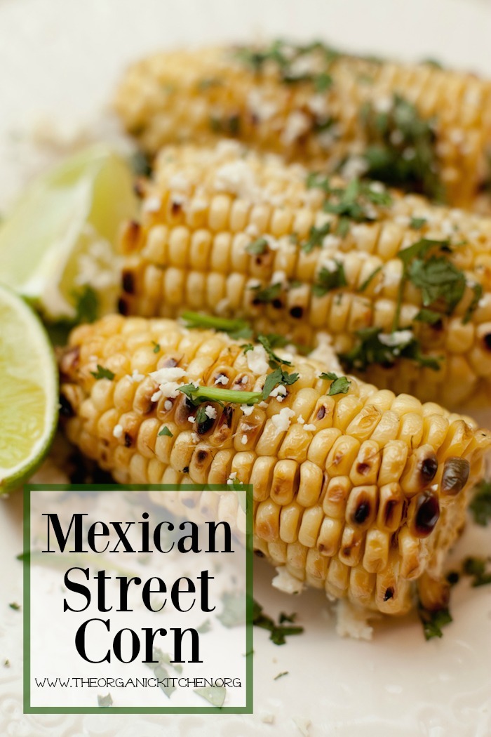 Three cobs of Mexican Street Corn with limes on white surface