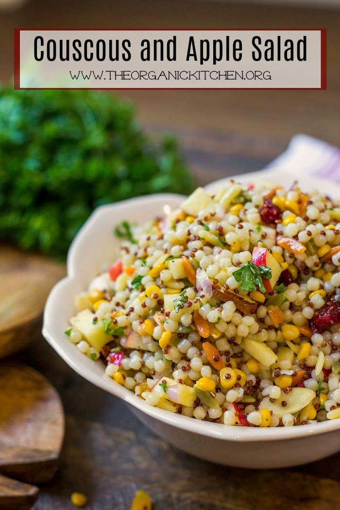 A pretty bowl of Couscous and Apple Salad on a wood surface with a bunch of parsley in backgraound