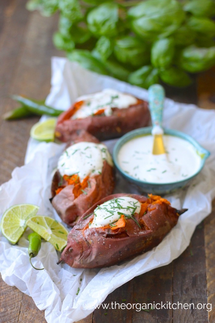 Baked Sweet Potatoes with Spicy Maple Creme Fraiche on white parhcment set on wood table, basil in the background