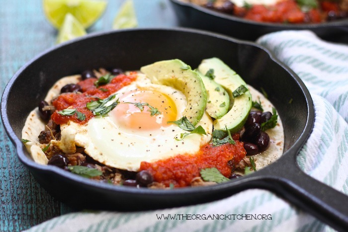 A close up of a single cast iron skillet filled with Easy Huevos Rancheros and slices of lime on a blue table