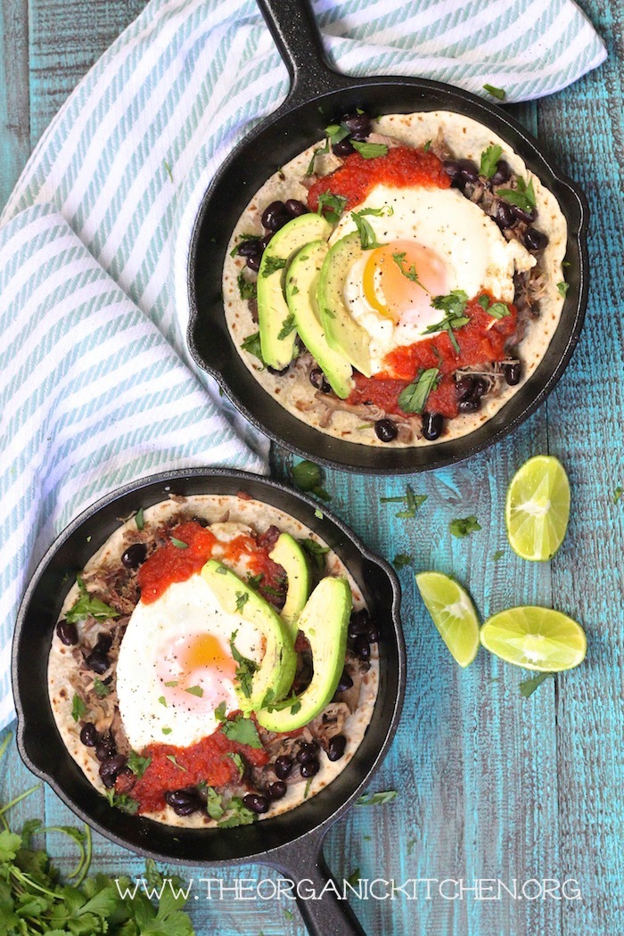 An aerial view of two pans filled with Easy Huevos Rancheros, a stripped dish towel, and lime wedges