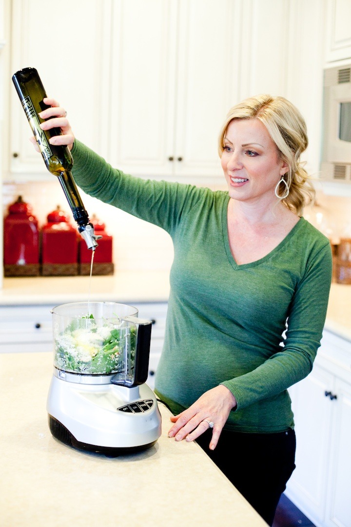A woman pouring olive oil in a food processor to make pesto