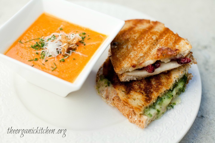 Creamy Carrot Tomato Soup ina white boiwl next to two grilled cheese sandwiches