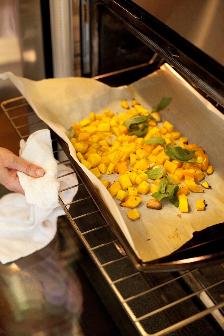 A woman pulling an oven rack out to check on the progress of roasting butternut squash used to make Homemade Butternut Squash Ravioli from The Organic Kitchen