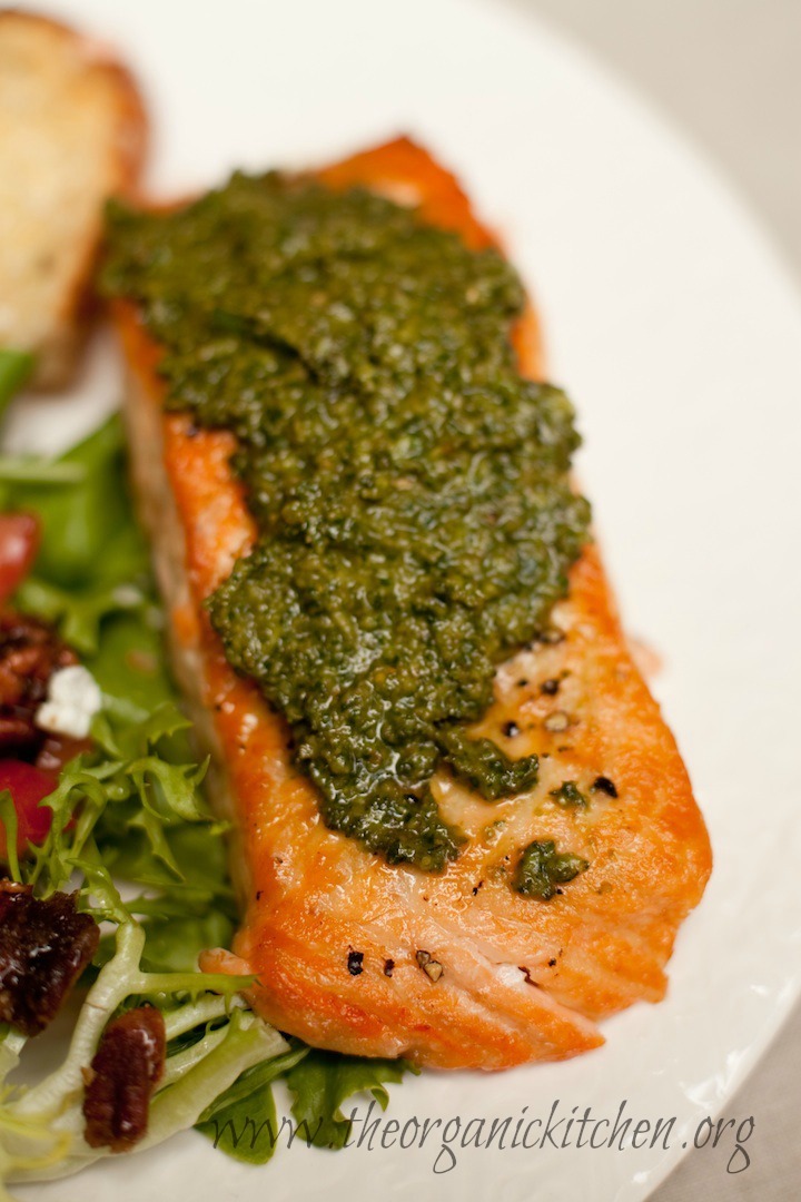 A salmon filet topped with fresh basil pesto on a white plate