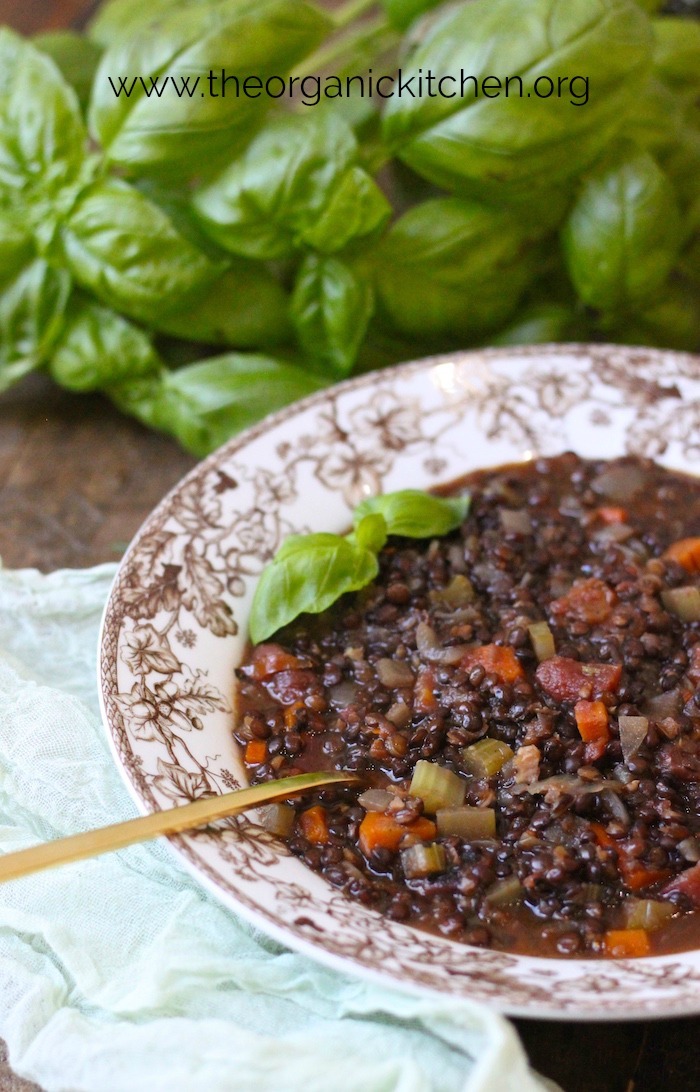 A bowl Hearty Lentil Soup with basil in the background