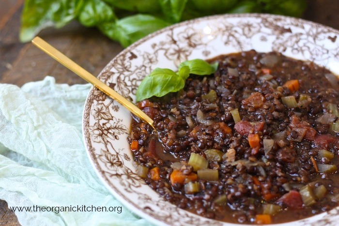 Hearty Lentil Soup in a white and brown holiday bowl with gold spoon garnished with basil