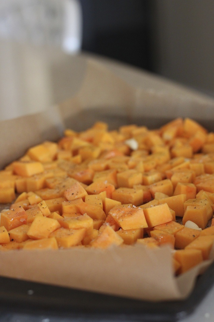 A cookie sheet covered with parchment paper and filled with diced butternut squash for use in Fall Greens with Roasted Butternut Squash and Spicy Pepitas 
