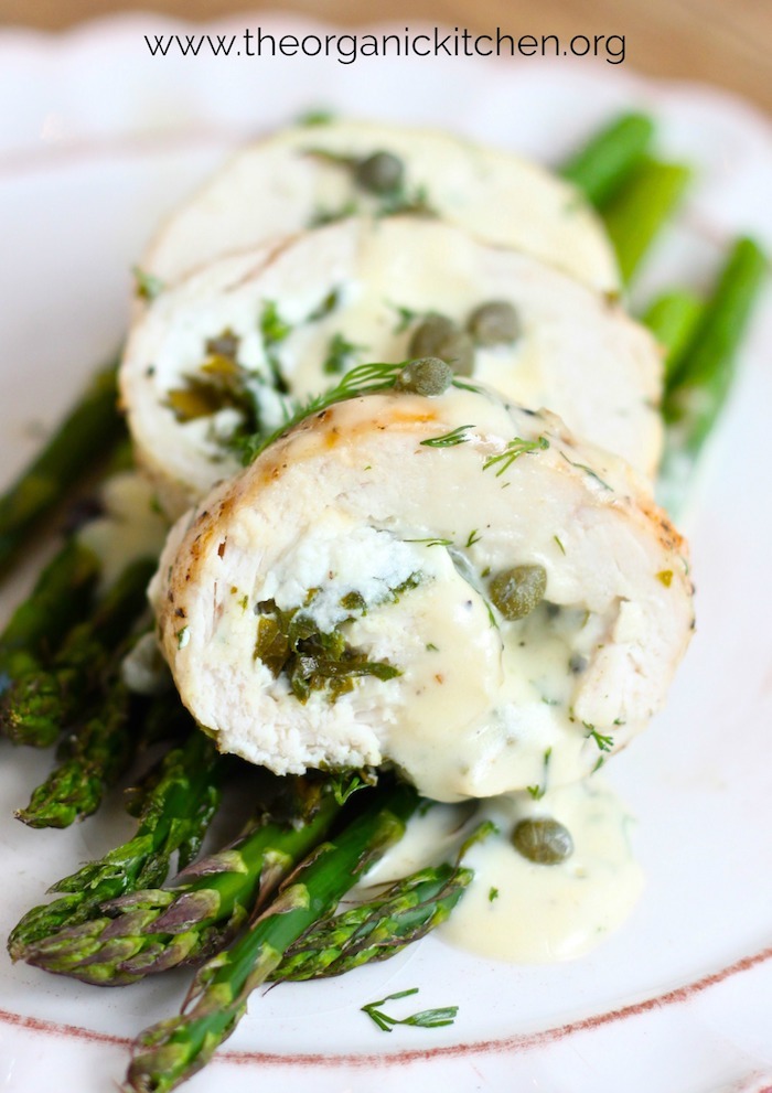 Spinach and Goat Cheese Stuffed Chicken Breasts on Asparagus with Dill Cream Sauce on small white plate garnished with dill and capers