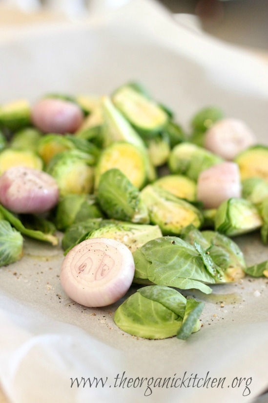 Fresh Brussels sprouts and shallots on a parchment covered cookie sheet in preparation for making , Roasted Brussels Sprouts with Apples and Hazelnuts