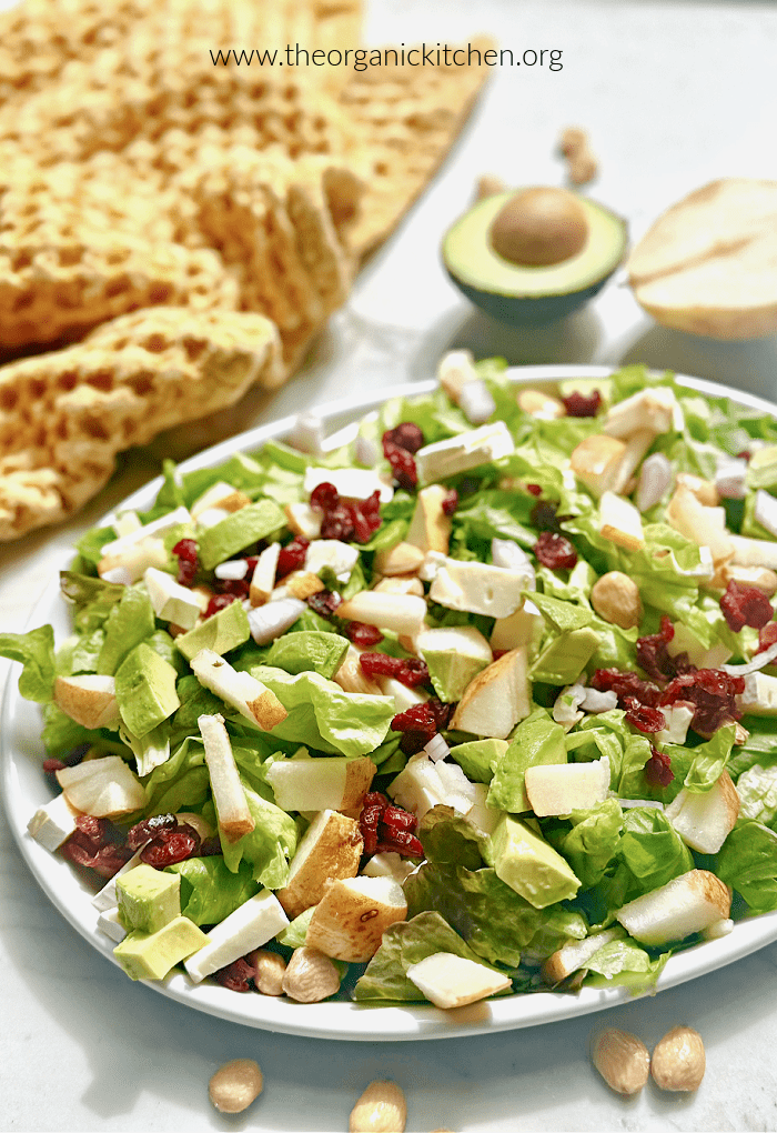 A green salad with brie, pears and cranberries on white plate with yellow dish towel in the background