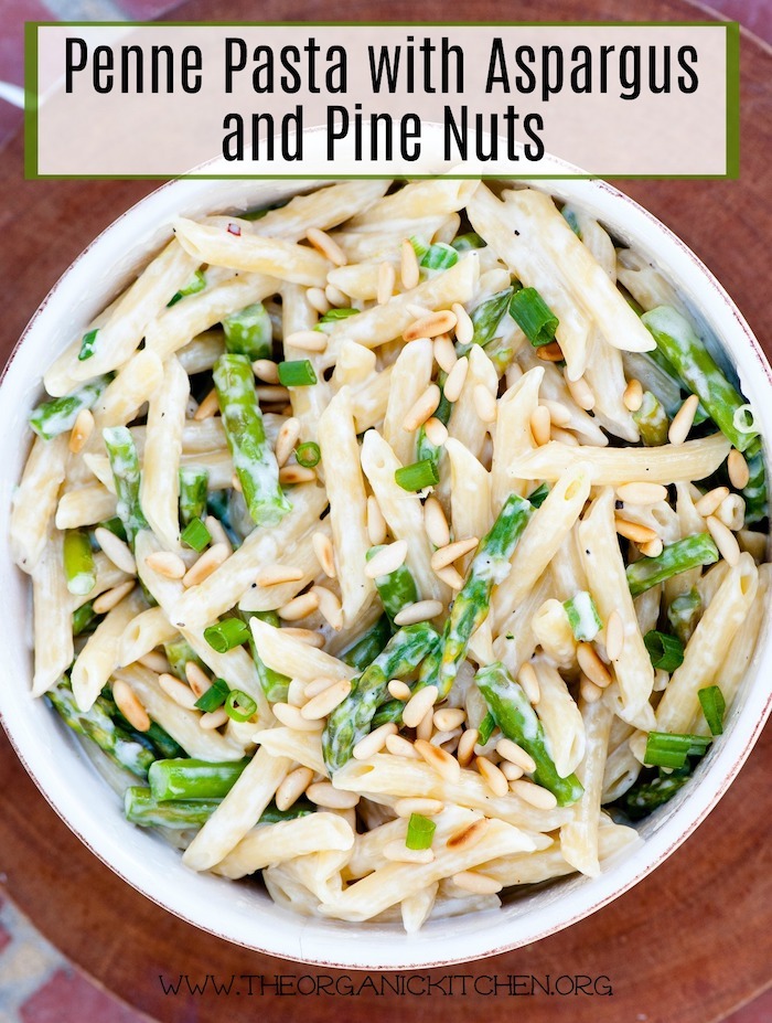 Penne Pasta with Asparagus and Pine Nuts in a big white bowl on wood cutting board