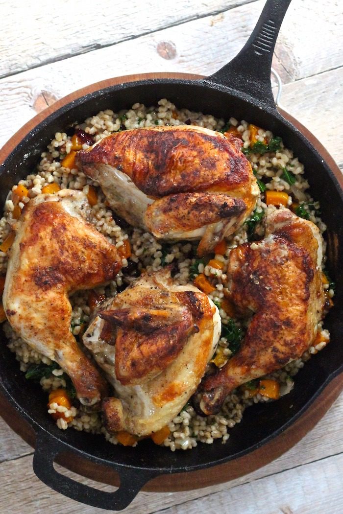 A black cast iron pan with roasted chicken and barley