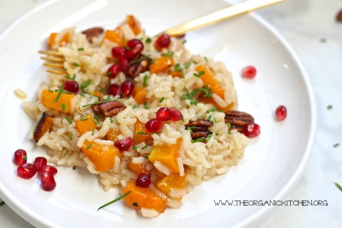 Roasted Butternut Squash Risotto with Candied Pecans garnished with pomegranate seeds and chives on white plate