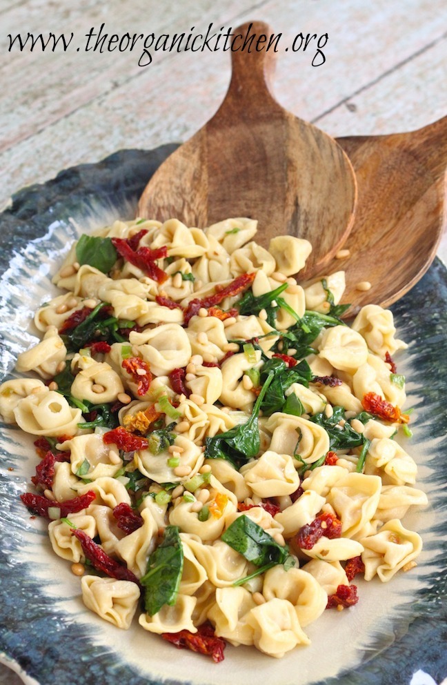 Three Cheese Tortellini with Spinach and Sun Dried Tomatoes on blue platter with wooden serving spoons