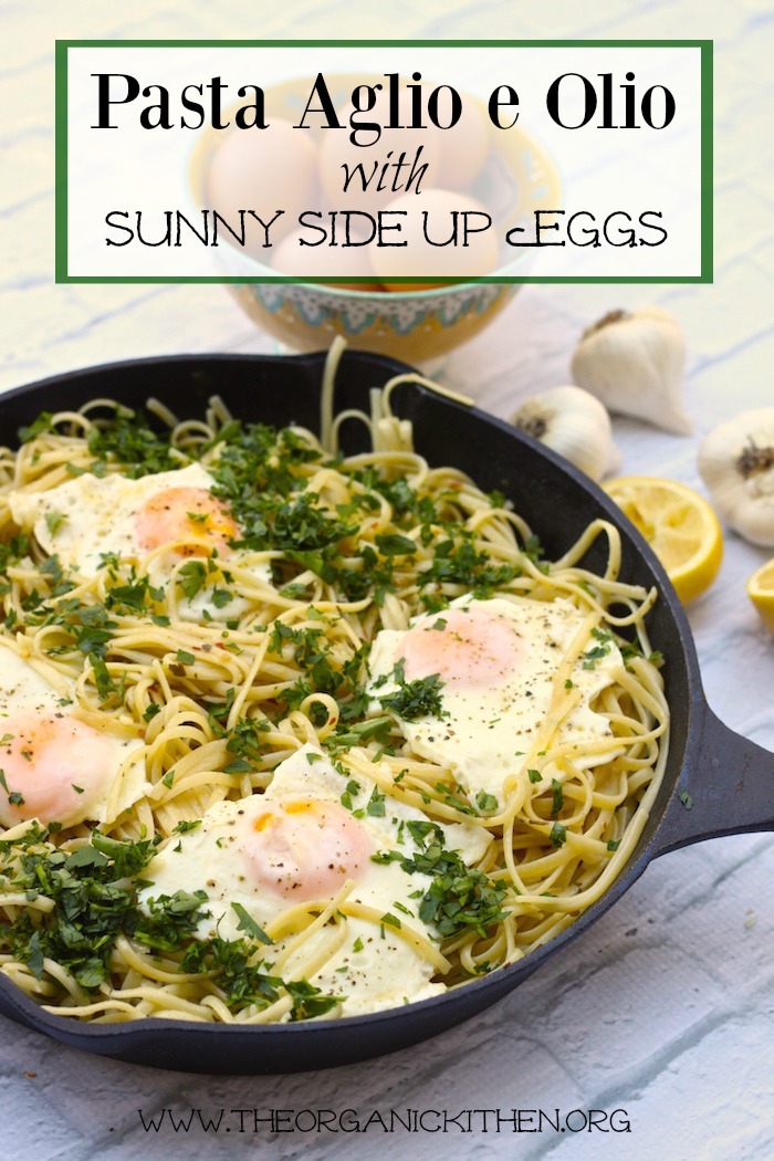 Pasta Aglio e Olio with Eggs Sunny Side Up in a black cast iron pan surrounded by garlic and lemons