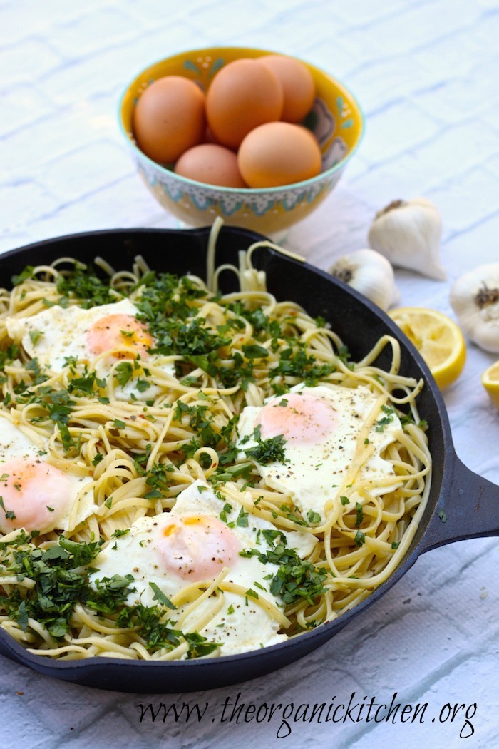 Pasta Aglio e Olio with Sunnyside Up Eggs in black cast iron pan with a bowl of eggs in the background