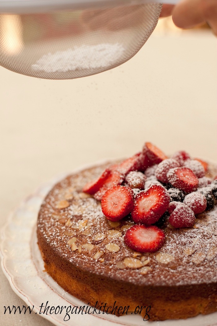 Traditional Olive Oil Cake with berries being dusted with powdered sugar