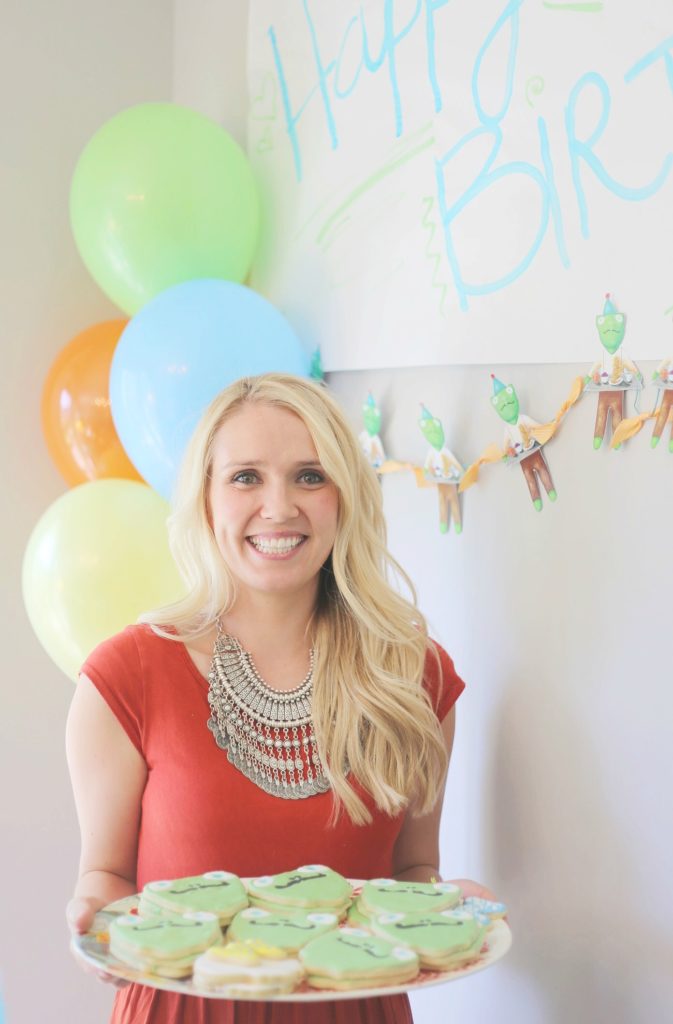 A woman holding a plate of cookies with balloons in the background
