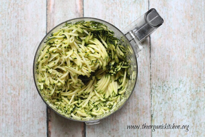 An aerial shot of food processor bowl with grated zucchini that will be used to make Zucchini Fritters with Lemon Ricotta (with Gluten Free Option)