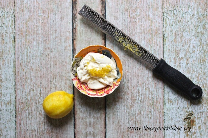 A small dish of ricotta cheese with lemon zest and microplane set on a wooden backdrop 