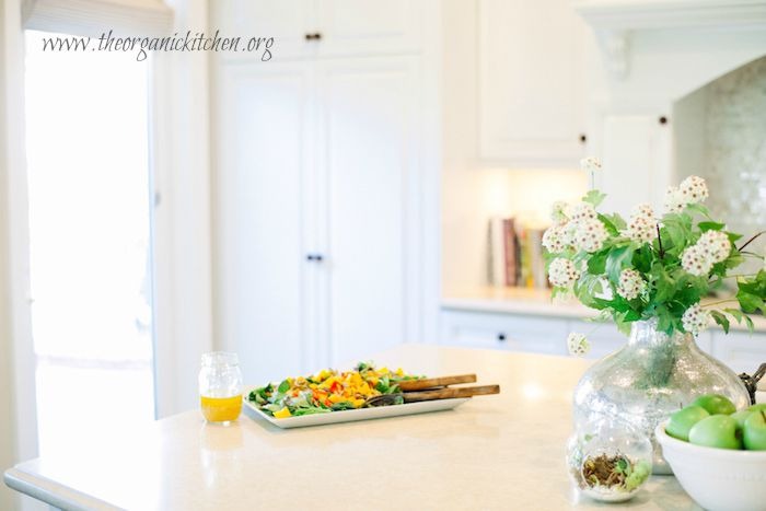 A beautiful white kitchen with a platter of Greens with Mango and Citrus Vinaigrette set on the counter
