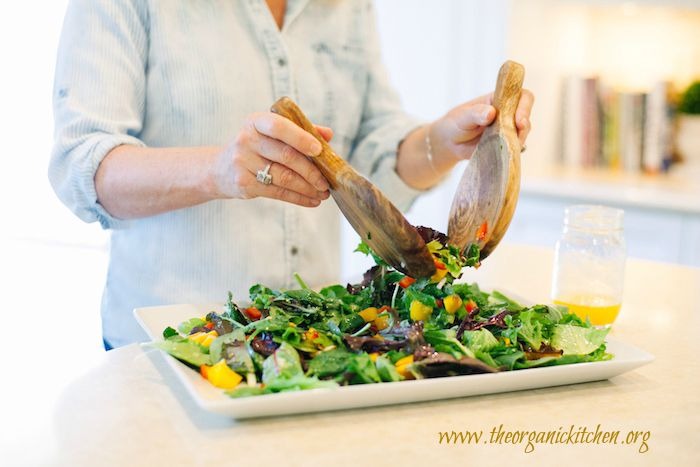A woman using two wooden tongs to toss Greens with Mango and Citrus Vinaigrette