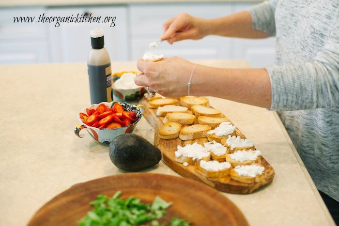 A woman spreading ricotta cheese in toasted baguette slices to make Strawberry and Avocado Bruschetta: Bruschetta 