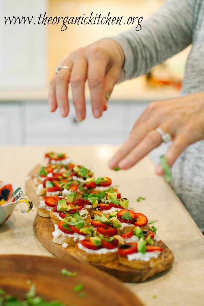 A woman garnishing Strawberry and Avocado Bruschetta with basil