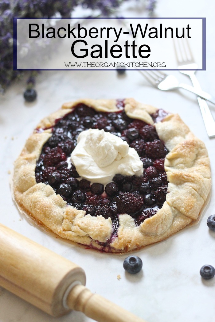 a beautiful Blackberry Walnut Galette with whipped cream surrounded by berries and a rolling pin