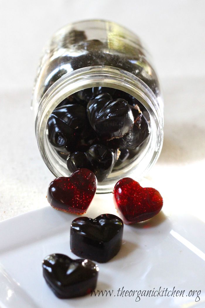 A jar lying on it's side with Pomegranate Gelatin Gummies spilling out onto a white background