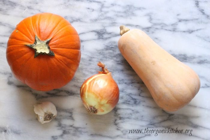 A small sugar pumpkin, butternut squash, onion and garlic on marble counter, ingredients for Savory Pumpkin Soup