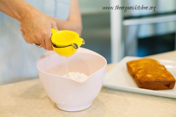 Two hands squeezing lemon juice into a pink bowl in preparation to make Lemon Vanilla Raspberry Cake