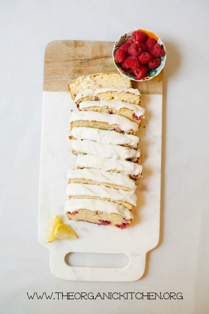 A sliced loaf Lemon Vanilla Raspberry Cake with lemon slices and bowl of raspberries on a platter
