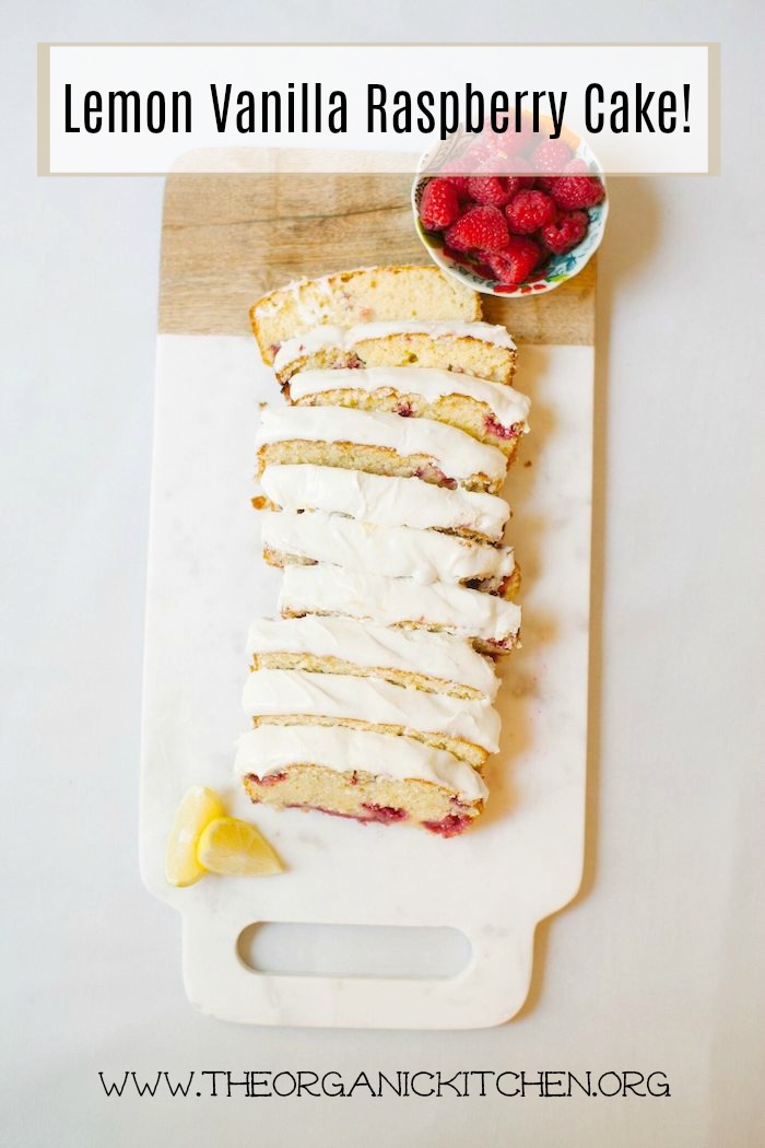 A sliced loaf of Lemon Vanilla Raspberry Cake with a small bowl of fresh raspberries