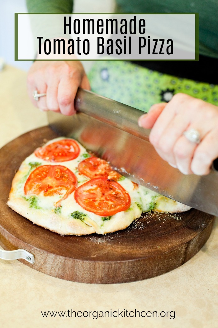 A woman's hands using a pizza cutter to slice a Fresh Tomato Basil Pizza 