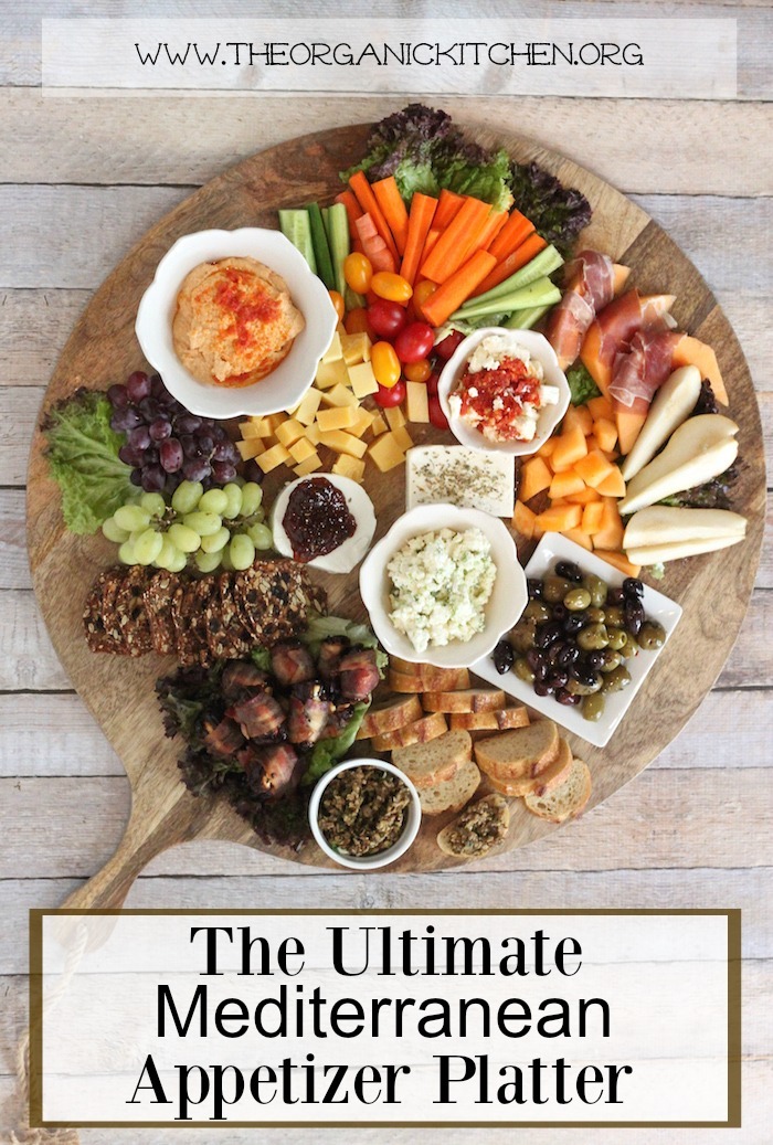 The ultimate Mediterranean appetizer platter filled with hummus, vegetables, cheeses and olives set on a wooden table