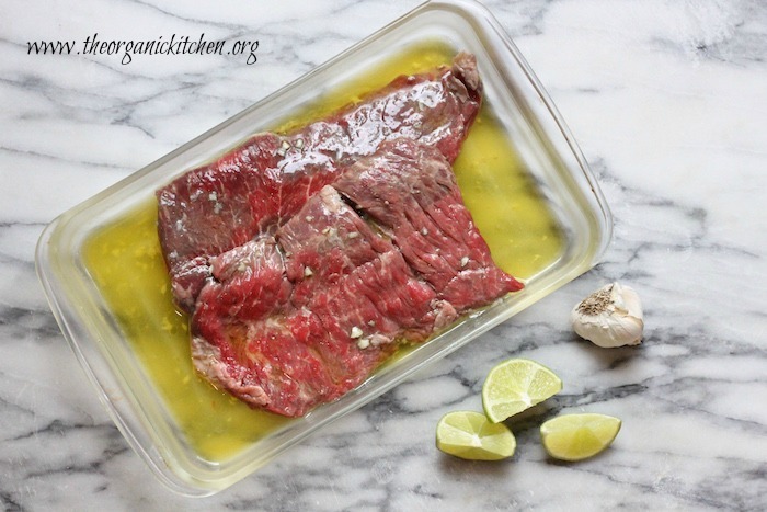 A clear baking dish with a steak marinating in oil: Grilled Skirt Steak and Veggies with Guacamole