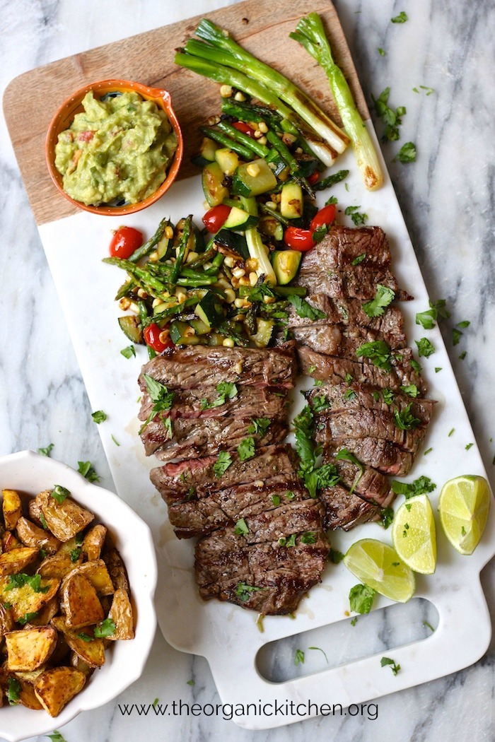 Grilled Skirt Steak and Veggies with Guacamole on a white marble cutting board