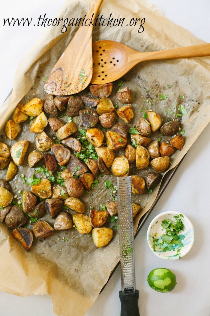 Roasted Mexican Potatoes with Cilantro Gremolata on a cookie sheet with lime and herbs