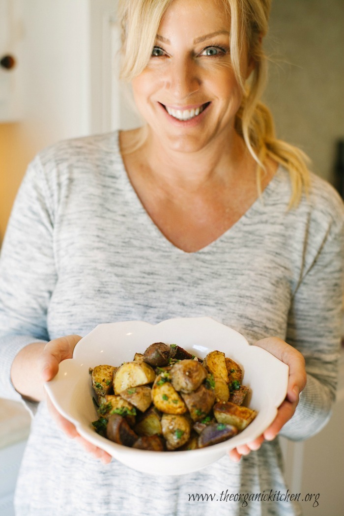 A blonde woman holding a bowl of Roasted Mexican Potatoes with Cilantro Gremolata