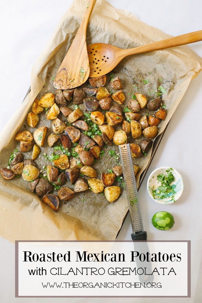 Crispy Roasted Mexican Potatoes with Cilantro Gremolata on a parchment covered cookie sheet with wooden tongs, microplane, and small bowl of herbs