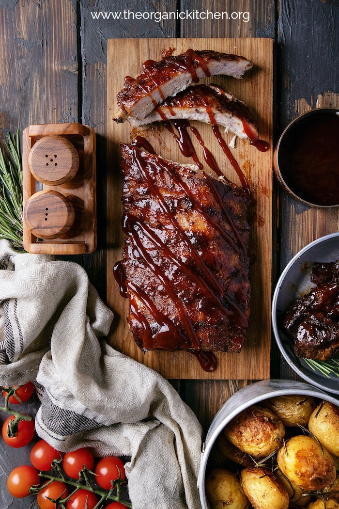 "BBQ" Baby Back Ribs (Instant Pot) on wood surface surrounded by bowls of vegetables and two salt and pepper skaers