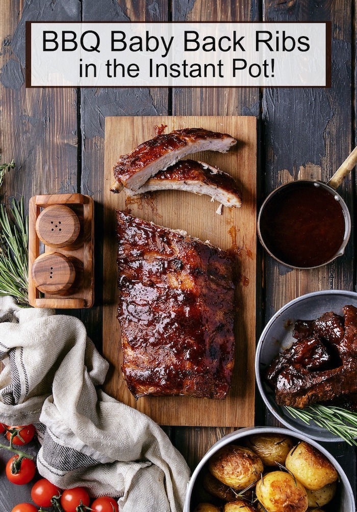 "BBQ" Baby Back Ribs (Instant Pot) set on a wooden cutting board surrounded by bowls of BBQ sauce, tomatoes, potatoes and herbs