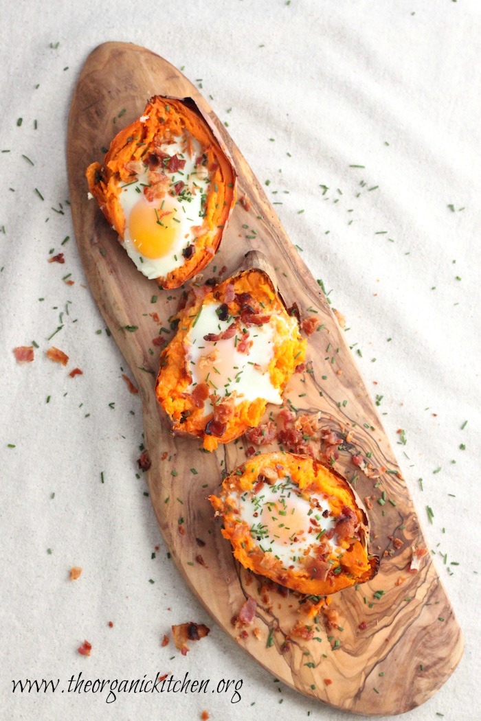 Three Twice Baked Sweet Potatoes with Bacon and Eggs on a wooden platter set on a  white cloth