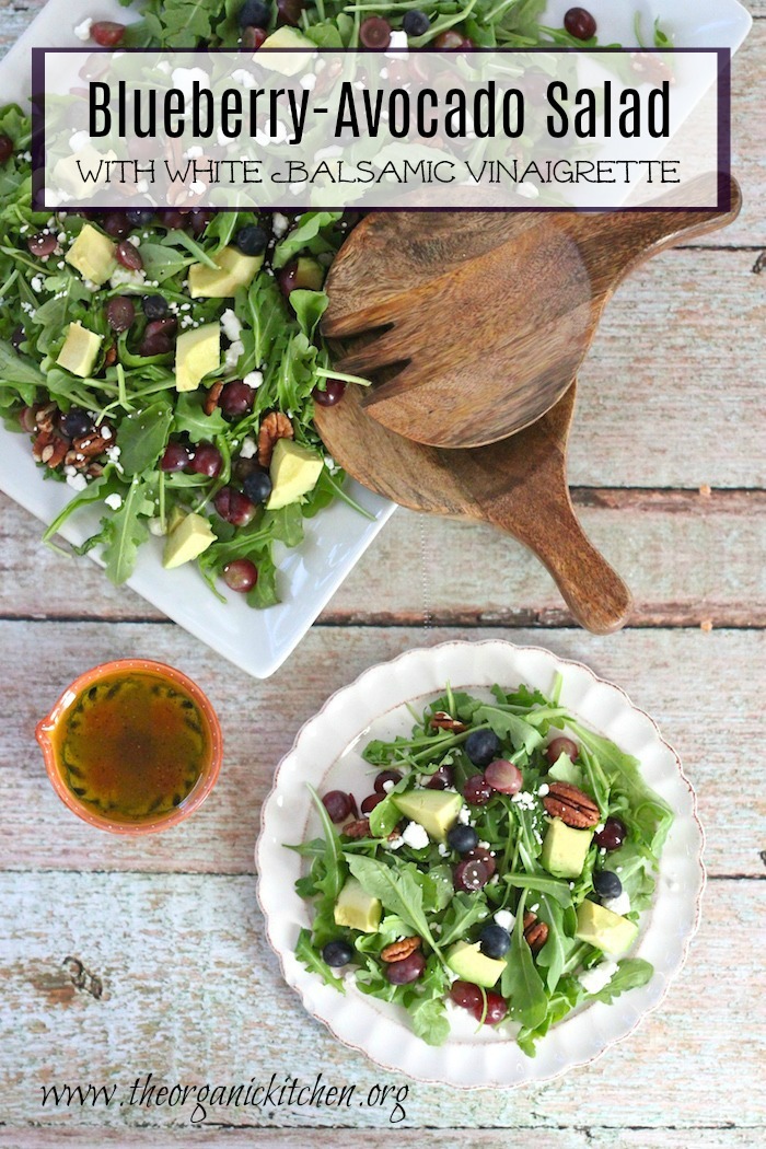 Blueberry and Avocado Salad on a white plate and white platter with wooden serving utensils