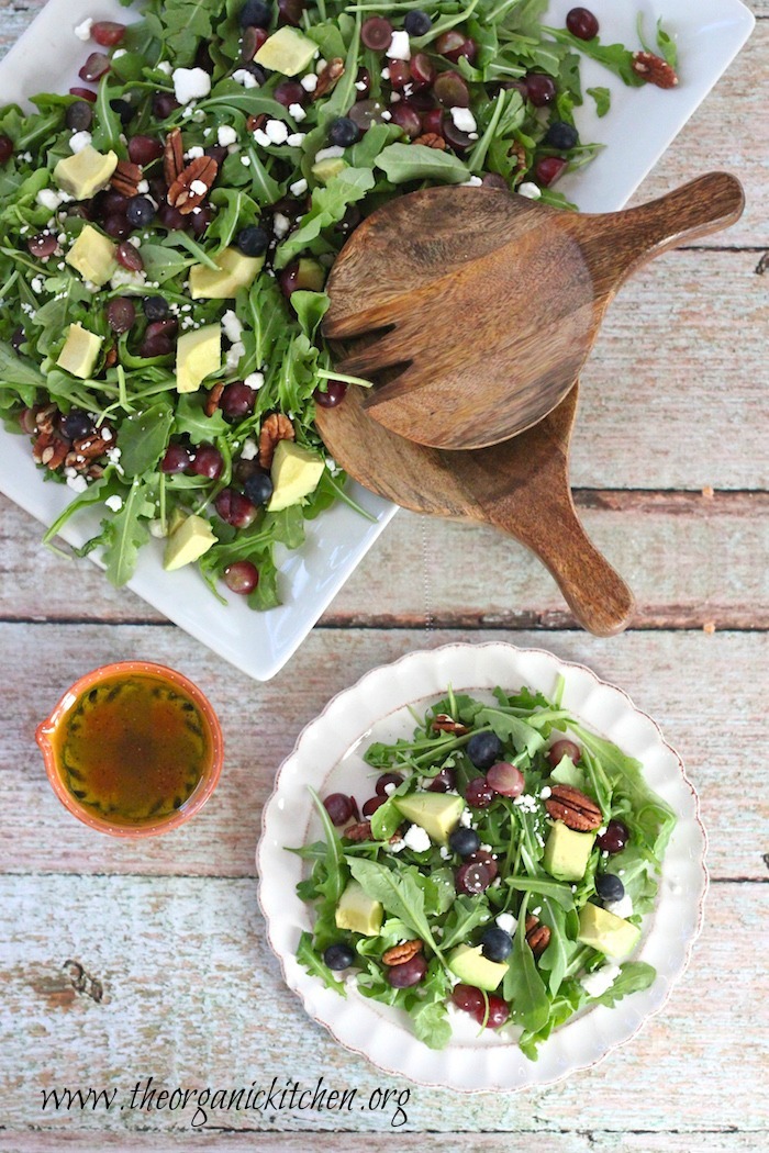 Blueberry and Avocado Salad on white dishes with a small bowl of salad dressing on a light green wooden backdrop