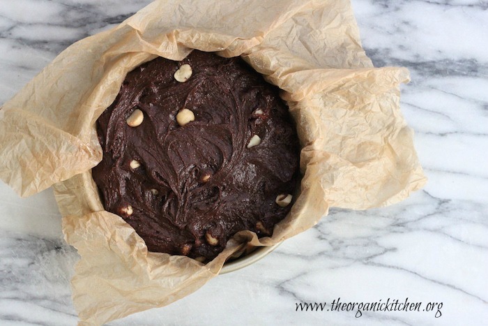 The batter for Brown Butter Brownies with Macadamia Nuts in a parchment paper lined cake pan